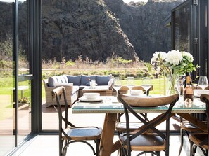 A dining area with a glass table, wooden chairs, and a sofa with cushions. There is a vase with flowers on the table. - Lambs Lodge (Bamburgh)