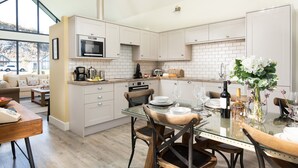 A modern kitchen with white cabinets, a glass dining table, and a view of the outside. - Lambs Lodge (Bamburgh)
