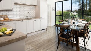 A modern kitchen with white cabinets, a wooden countertop, and a dining area with a table set for six. - Lambs Lodge (Bamburgh)