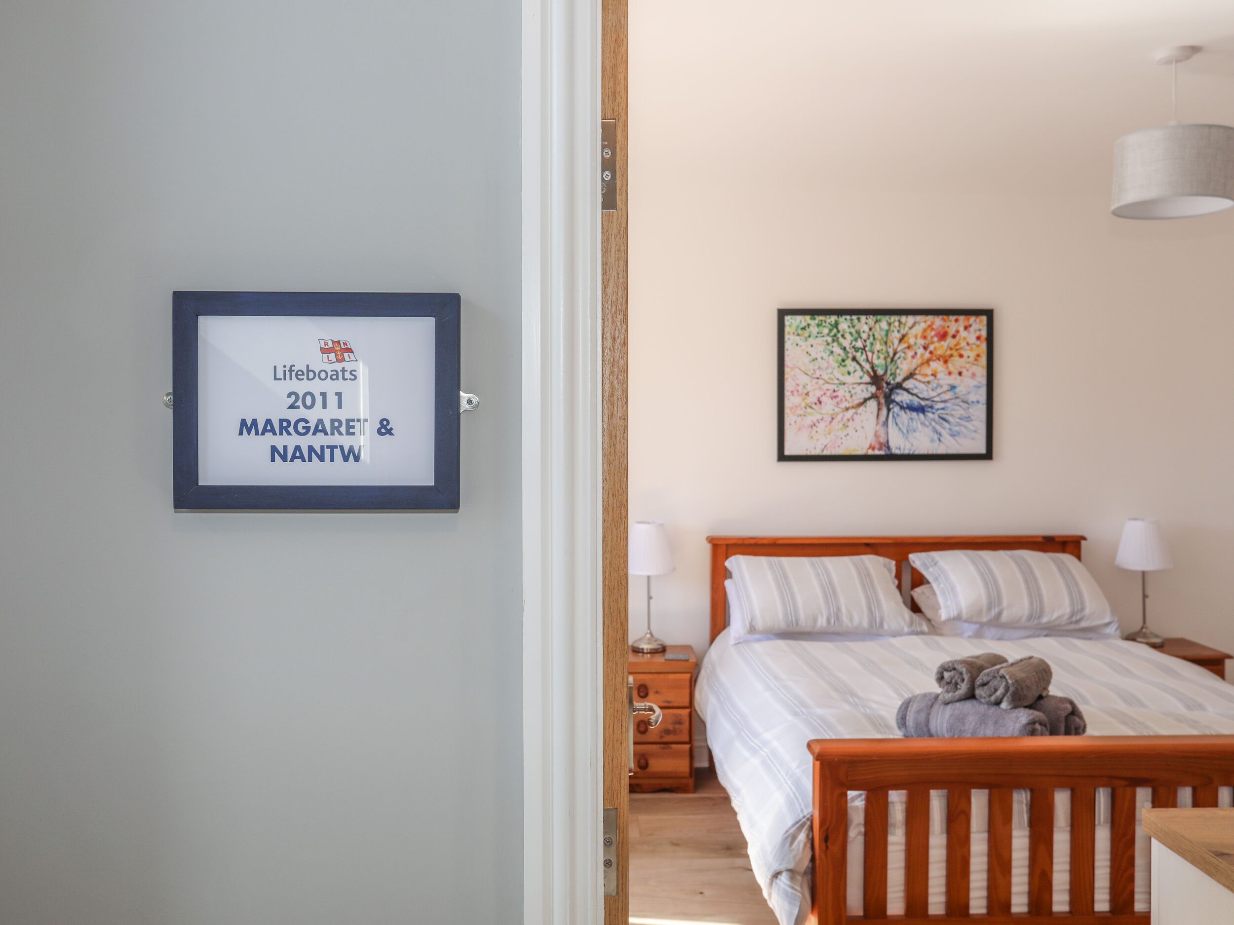 Un dormitorio con cama, mesita de noche, lámpara y un certificado enmarcado en la pared.
