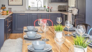 A modern kitchen with dark cabinets, a wooden dining table set with plates, bowls, and wine glasses, and a Chilean pepper poster on the wall. - Cambrian House (Criccieth)