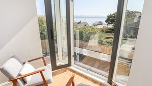 A balcony with two chairs and a wooden floor, overlooking a residential area with houses and a body of water. - Cambrian House (Criccieth)