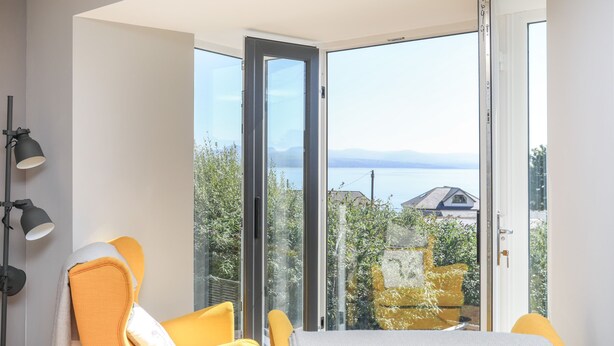 A modern room with a large sliding glass door leading to a balcony with a view of the sea and mountains. - Cambrian House (Criccieth)
