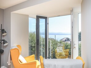 A modern room with a large sliding glass door leading to a balcony with a view of the sea and mountains.