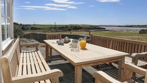 Ein Holztisch mit Bänken auf einer Terrasse mit Blick auf ein Gewässer und hügelige Landschaft.