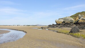 Ein sandiger Strand mit Felsformationen und blauem Himmel.