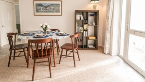 Un coin repas avec une table ronde, des chaises, un tableau encadré, une bibliothèque et une fenêtre avec des rideaux.