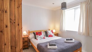 Une chambre à coucher avec un lit en bois, deux tables de chevet avec des lampes, une fenêtre avec des rideaux et un luminaire suspendu.