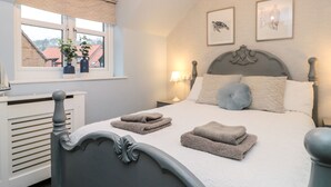 A neatly made bed with two folded towels, a bedside lamp, and a window with a view of buildings. - Fauna's Corner (Whitby)