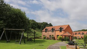 A brick building with a gravel path leading to it, surrounded by greenery and a swing set. - Fauna's Corner (Whitby)