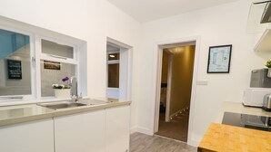 Une cuisine moderne avec des meubles blancs, un évier en acier inoxydable et un plan de travail en bois. On y trouve un four à micro-ondes et un grille-pain posés sur le plan de travail.