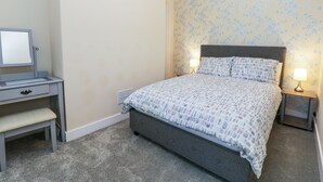 A bedroom with a bed, bedside tables, a desk, and a chair.