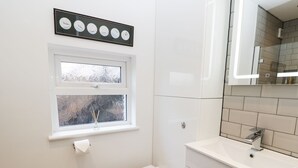 A bathroom with a toilet, a sink, a mirror, and a window with frosted glass.
