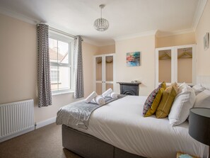 A bedroom with a bed, a radiator, a fireplace, a wardrobe, and a painting on the wall. - Wey Cottage (Weymouth)