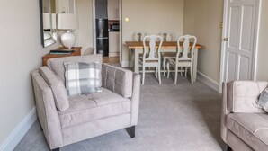 Ett vardagsrum med en soffa, ett matbord med stolar, ett kök i bakgrunden och en dörr.