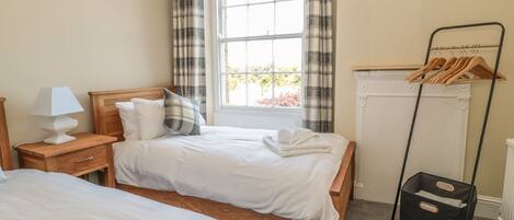 Une chambre d’hôtel avec deux lits, une table de chevet avec une lampe, un radiateur et un porte-vêtements.