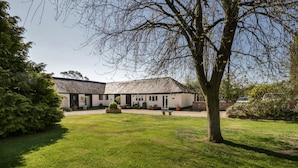 A building with a white exterior and a sloped roof, surrounded by a well-maintained lawn and trees. - Orchard Cottage (Shaftesbury)