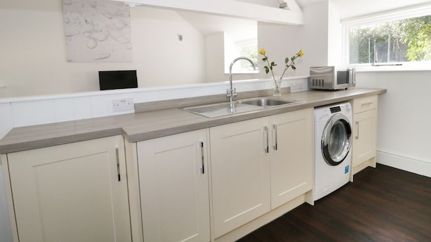 A modern kitchen with a built-in washing machine, a sink, and a window providing natural light. - Orchard Cottage (Shaftesbury)