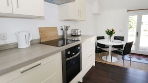 A modern kitchen with white cabinets, a black stove, and a dining area with a white table and chairs. - Orchard Cottage (Shaftesbury)