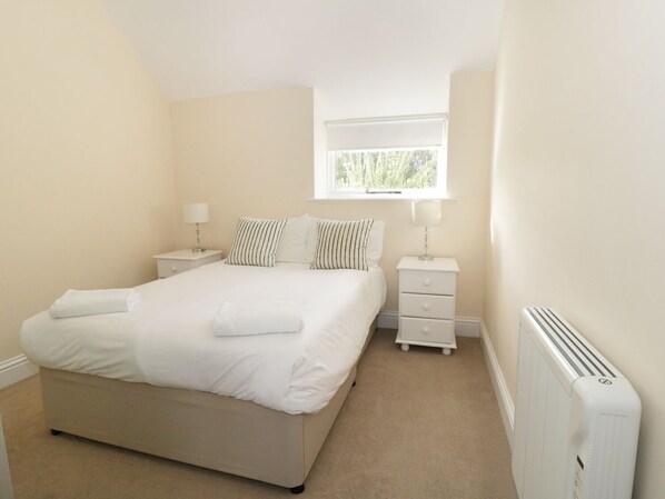 A bedroom with a bed, two bedside tables, a window, and a radiator.