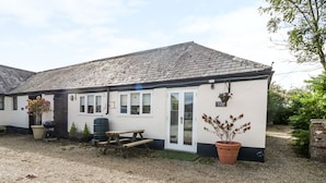 A cottage with a gravel driveway, a wooden bench, a picnic table, a barbecue grill, and a large potted plant. - Orchard Cottage (Shaftesbury)