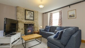 A living room with a stone fireplace, a grey sofa, a wooden coffee table, and a television on a white cabinet. - Brimpts Cottage (Yelverton)