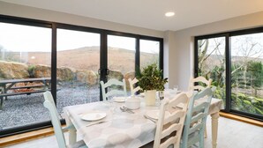 A dining area with a table set for four, large windows, and a view of a rocky landscape. - Brimpts Cottage (Yelverton)