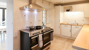 A modern kitchen with a stainless steel stove, oven, and a range hood. There is a wooden countertop and a sink with a faucet. The kitchen has white cabinets and a tiled backsplash. - Brimpts Cottage (Yelverton)