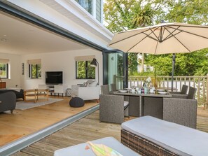Un salon moderne doté d’un téléviseur, d’un canapé et d’un coin repas, avec des meubles en osier et un grand parasol.