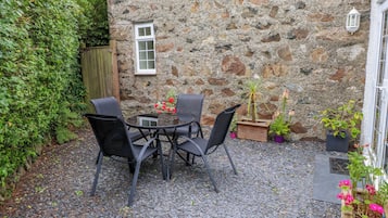 A stone wall with a window, a round table with chairs, and potted plants.