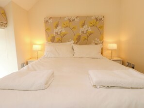 Un lit bien fait, avec deux oreillers et deux serviettes pliées, de part et d’autre duquel se trouvent des lampes de chevet sur une table de nuit.