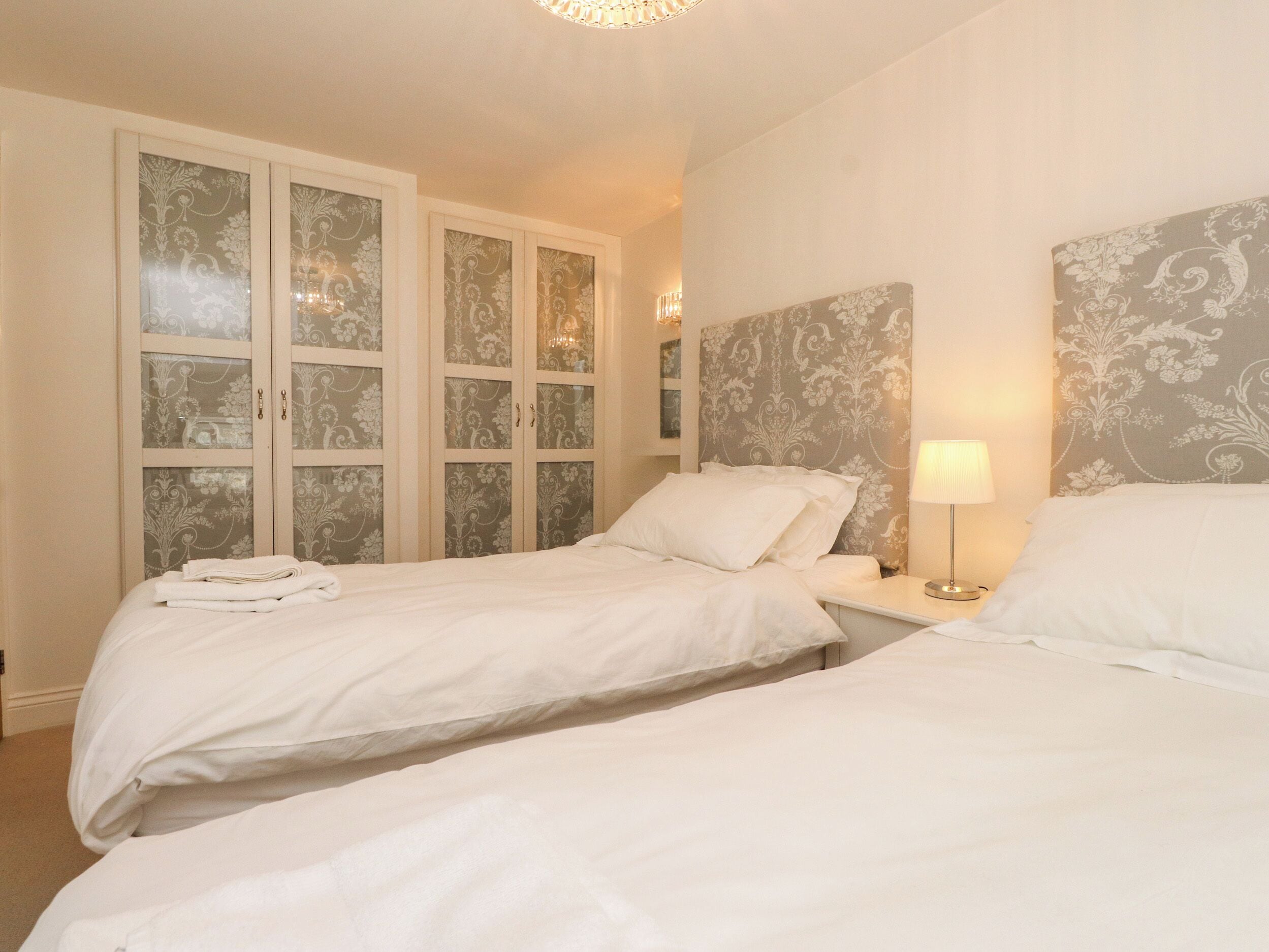 Una habitación de hotel con dos camas, un armario con puertas de cristal satinado y una lámpara de noche.