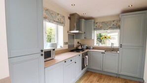 A kitchen with light blue cabinets, a microwave, a stove, and a window with a view of greenery. - Tan Y Goeden (Pwllheli)