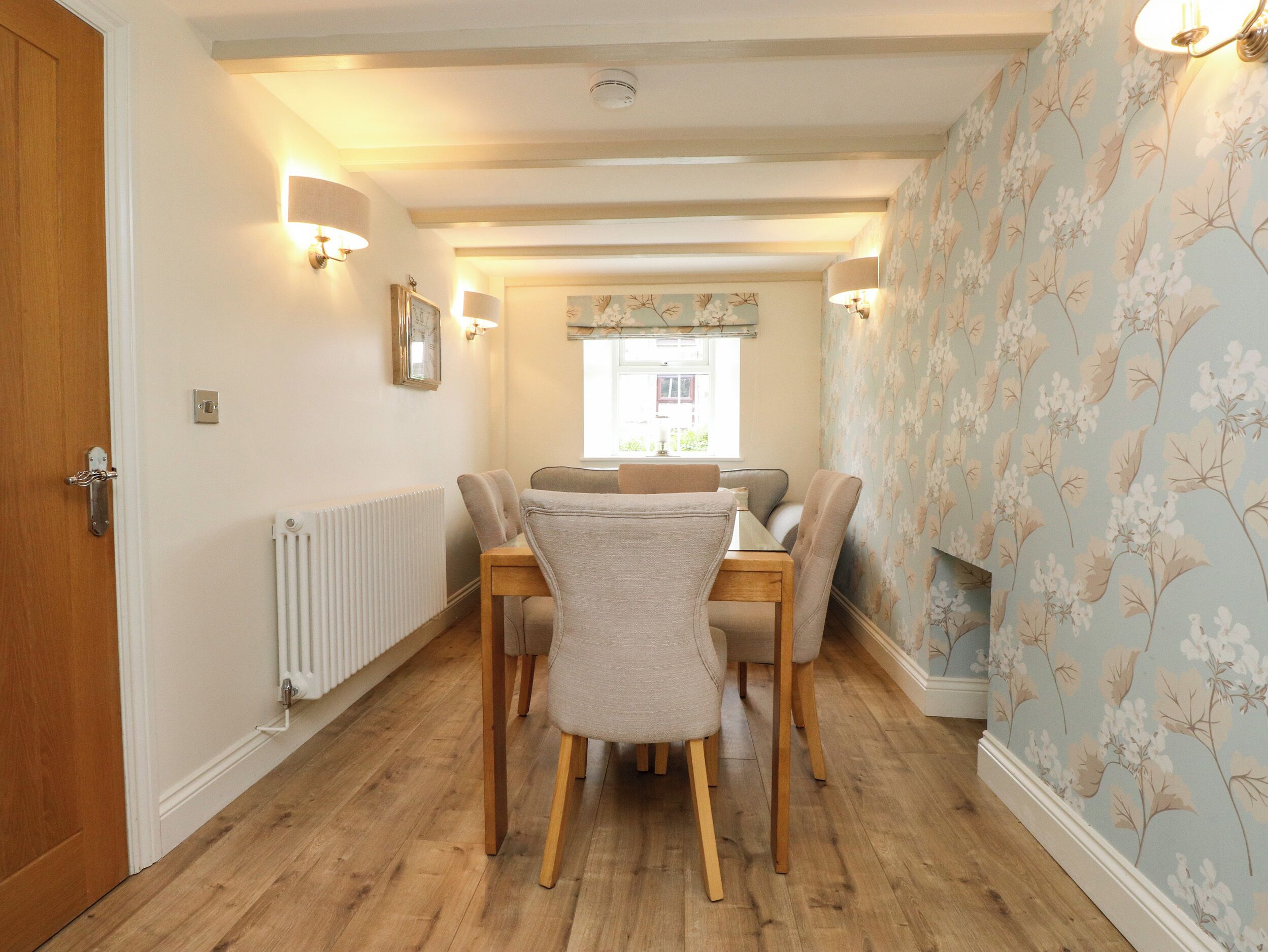 A dining area with a wooden table and chairs, a radiator, and a floral wallpaper pattern on the walls.