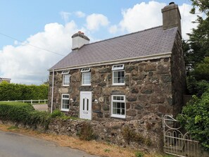 A stone house with a white door and multiple windows, surrounded by a fence and greenery. - Tan Y Goeden (Pwllheli)