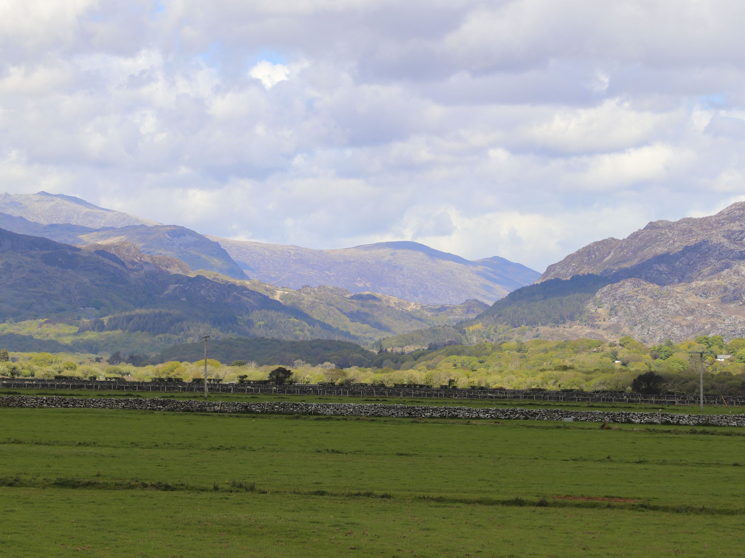 A mountainous landscape with a stone wall in the foreground and a clear sky.