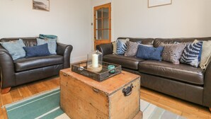 A living room with two leather sofas, a wooden coffee table, and a chandelier. - Cecily Cottage (Bideford)