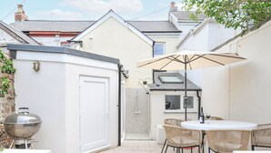 A patio area with a barbecue grill, outdoor seating, and a covered table. - Cecily Cottage (Bideford)