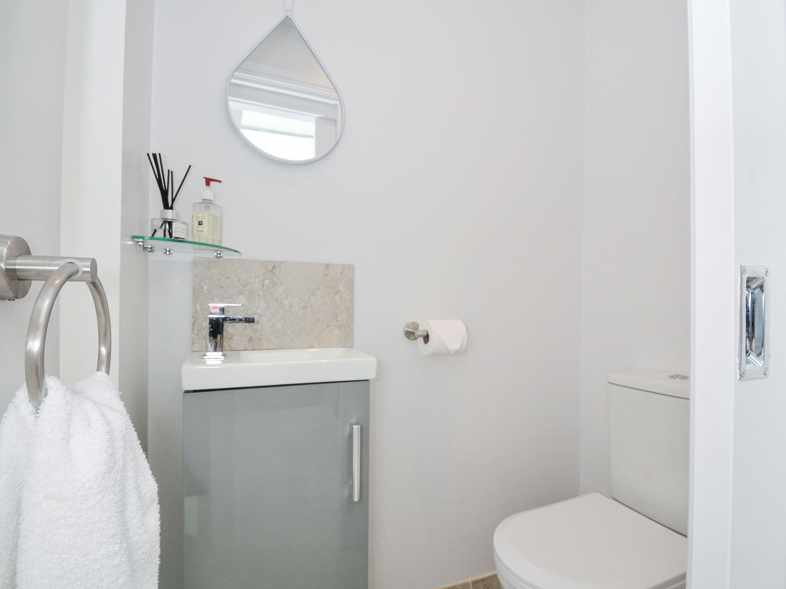 A bathroom with a toilet, a sink with a mirror above it, and a towel hanging on a metal ring.