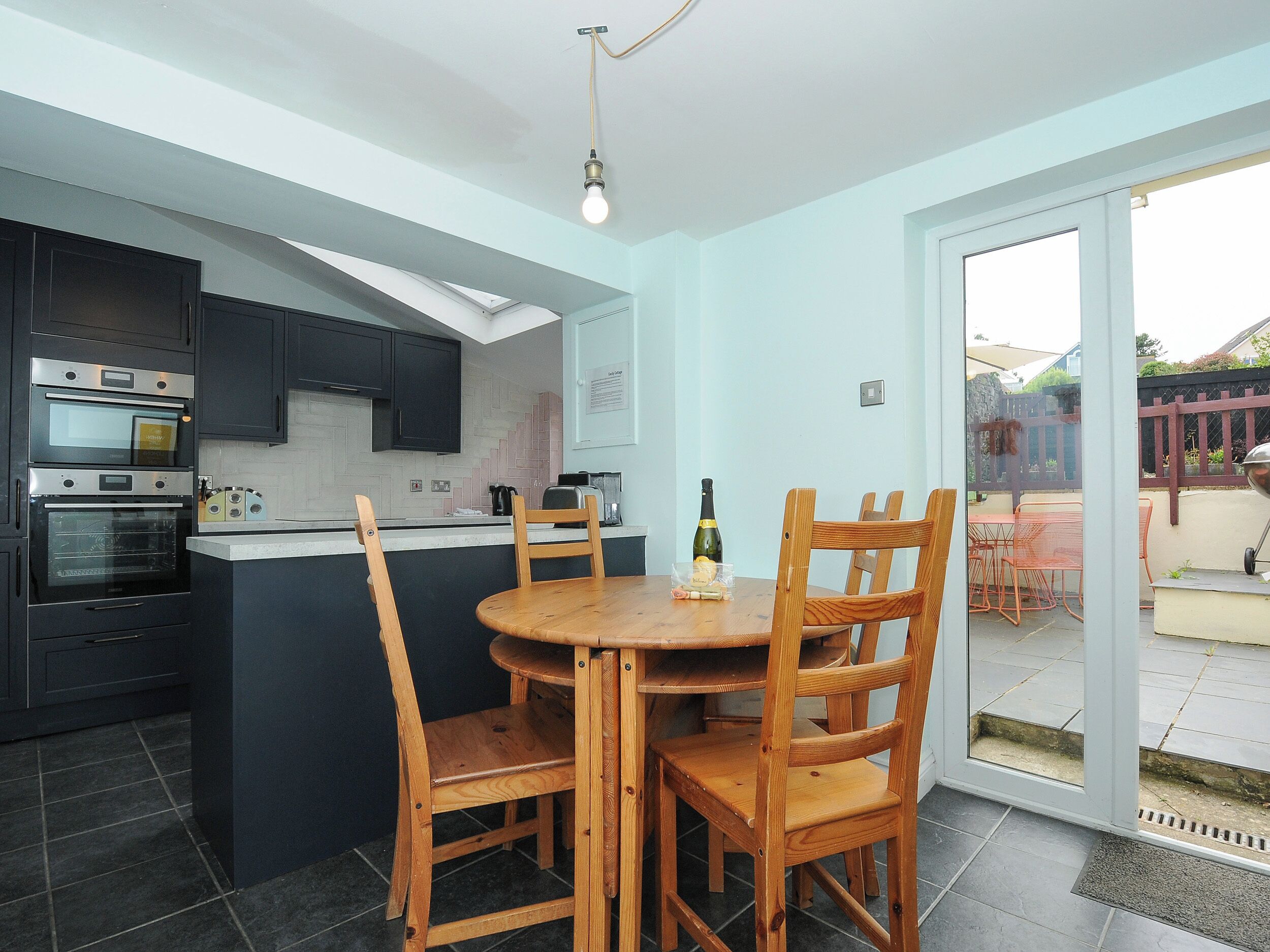 A modern kitchen with built-in ovens, a dining area with wooden chairs, and a sliding glass door leading to an outdoor patio.