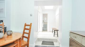 A modern kitchen with a wooden dining table and chairs, a built-in oven, and a view into the adjacent bathroom.