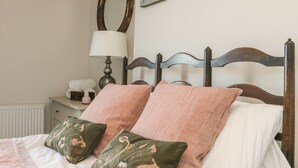 A bed with two pillows, a nightstand with a lamp, and a mirror on the wall. - Cecily Cottage (Bideford)