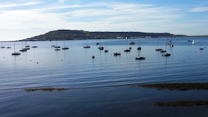 Ein Küstenblick mit mehreren Booten, die in ruhigem Wasser vor Anker liegen, einem entfernten Hügel mit Gebäuden und einem klaren Himmel.