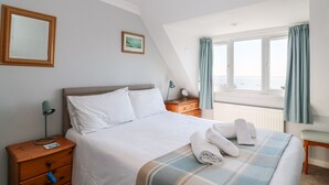 Ein Hotelzimmer mit Bett, Nachttisch, Kommode, einem Fenster mit Vorhängen und Meerblick.