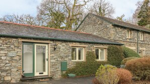 A stone cottage with a green door, a small porch, and a stone wall. - Apple Tree Cottage (Windermere)
