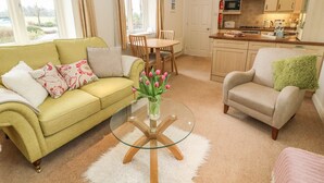A living room with a sofa, armchair, and a glass coffee table with a vase of flowers. - Apple Tree Cottage (Windermere)