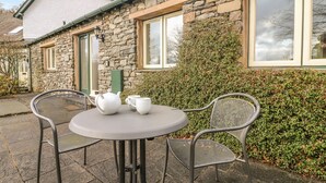 A stone house with a small patio area featuring a round table and two chairs. - Apple Tree Cottage (Windermere)
