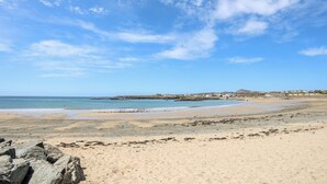 A beach with clear skies, rocky foreground, and distant buildings. - Tyn Towyn - Ty Glas Golau (Holyhead)