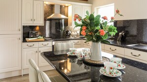 A kitchen with white cabinets, a black countertop, a stainless steel sink, and a wooden ceiling. - Tyn Towyn - Ty Glas Golau (Holyhead)