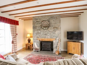 A cozy living room with a stone fireplace, wooden beams, a television, and a patterned rug.
